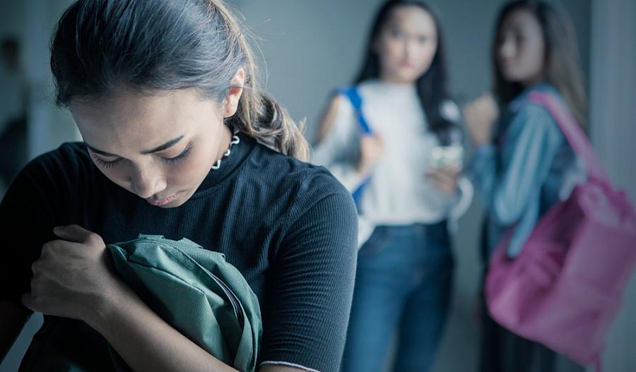 adolescente-abraza-su mochila-mostrando-tristeza-mientras-otras-dos-adolescentes-la-miran