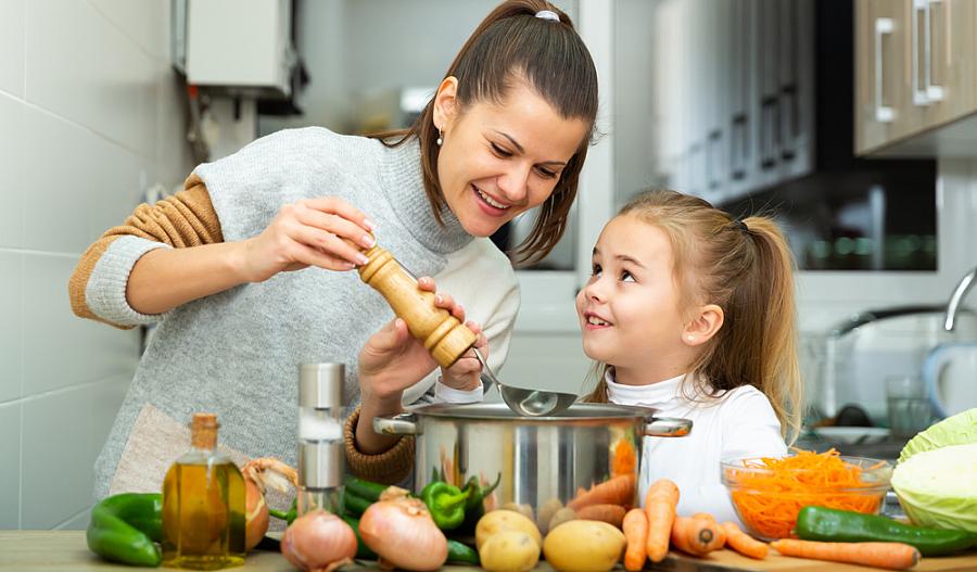 Fotografía de una madre cocinando comida saludable junto su hija pequeña.